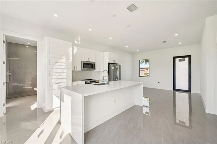 Kitchen featuring white cabinetry, a kitchen island with sink, light stone countertops, appliances with stainless steel finishes, and a breakfast bar area