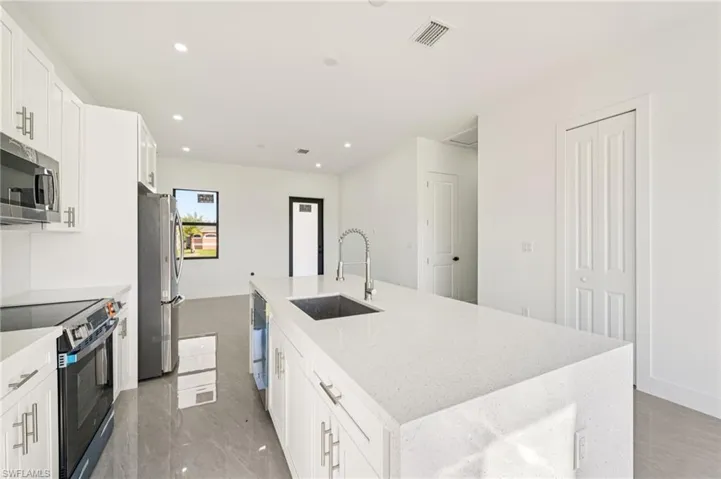 Kitchen with white cabinets, stainless steel appliances, light stone countertops, recessed lighting, and a center island with sink