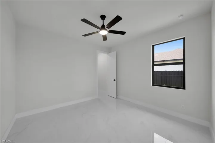 Empty room with marble look tile flooring, baseboards, and a ceiling fan