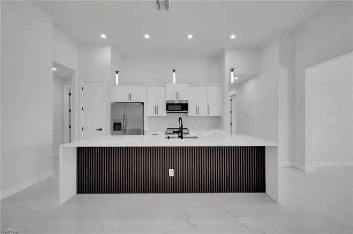Kitchen featuring stainless steel appliances, light marble finish flooring, a large island with sink, white cabinets, and a sink