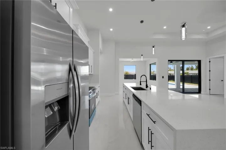 Kitchen with stainless steel appliances, a sink, white cabinetry, recessed lighting, and a large island with sink