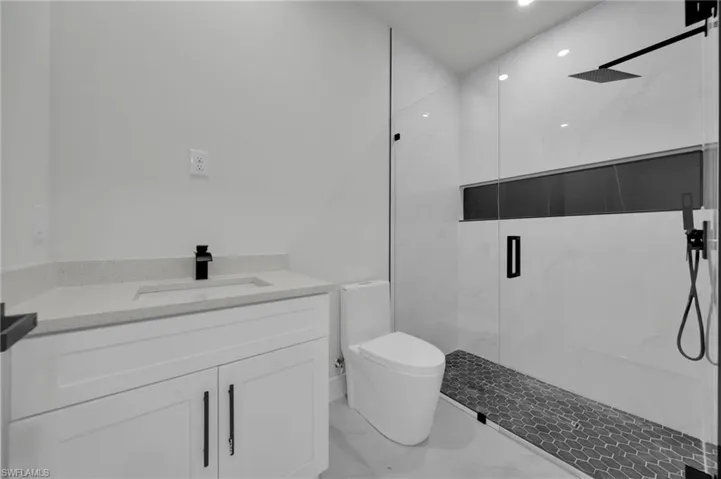 Full bathroom featuring marble finish floors, a marble finish shower, toilet, vanity, and recessed lighting