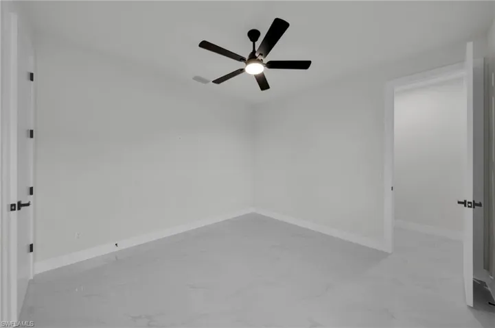 Spare room with marble look tiles, a ceiling fan, and baseboards