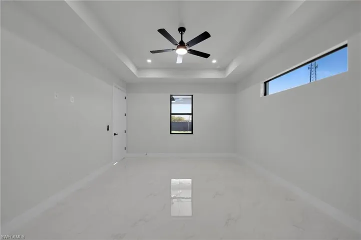 Empty room featuring light marble finish floors, baseboards, a tray ceiling, recessed lighting, and a ceiling fan