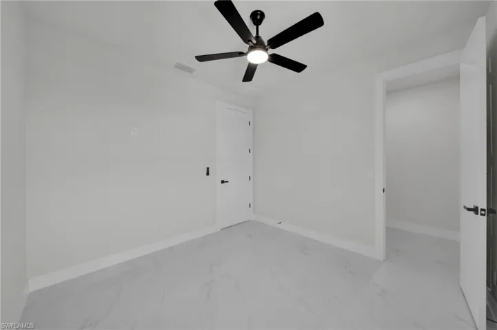 Empty room with light marble finish floors, a ceiling fan, and baseboards