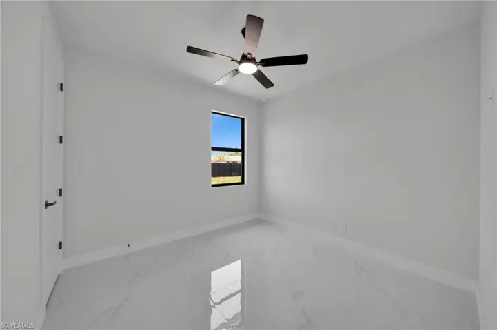 Spare room featuring marble look tiles, baseboards, and ceiling fan
