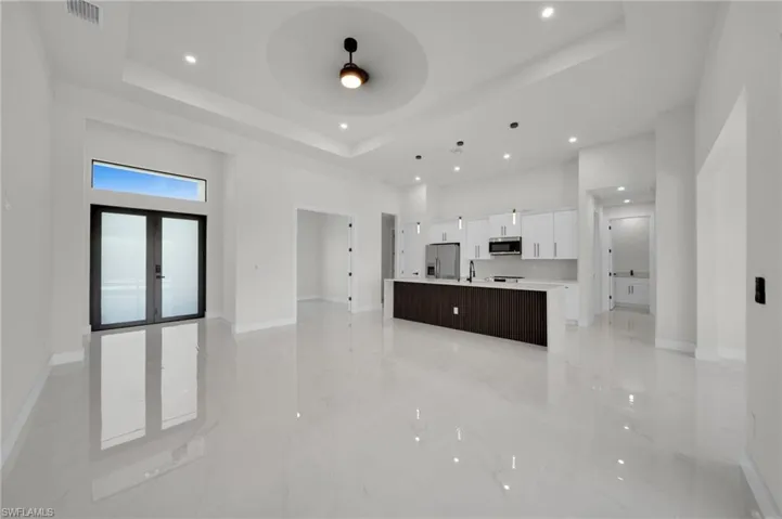 Unfurnished living room featuring a tray ceiling, a high ceiling, recessed lighting, baseboards, and ceiling fan