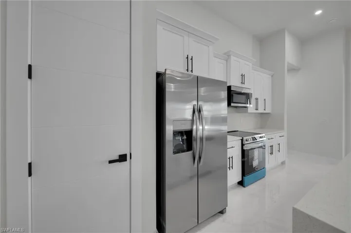 Kitchen featuring stainless steel appliances, light marble finish floors, light countertops, white cabinets, and recessed lighting