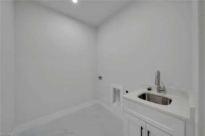 Washroom with electric dryer hookup, cabinet space, light marble finish floors, hookup for a washing machine, and baseboards