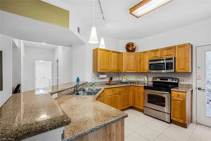 Kitchen featuring appliances with stainless steel finishes, a peninsula, light stone countertops, and hanging light fixtures
