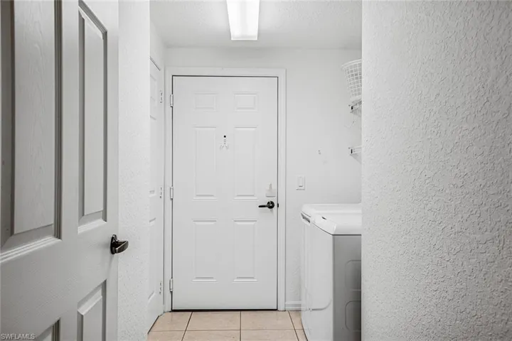 Laundry room featuring light tile patterned floors, separate washer and dryer, and a textured wall