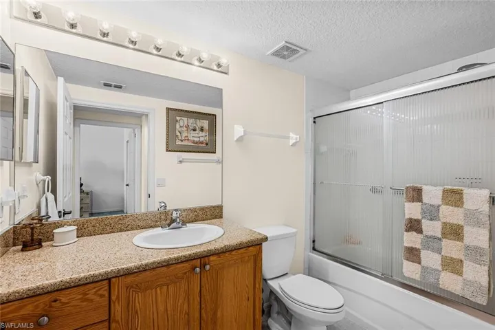 Bathroom with vanity, enclosed tub / shower combo, and a textured ceiling