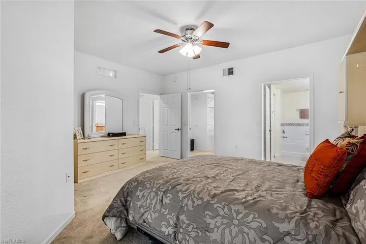 Bedroom with light colored carpet, connected bathroom, a spacious closet, and ceiling fan