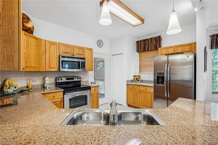 Kitchen with stainless steel appliances, backsplash, pendant lighting, and brown cabinets