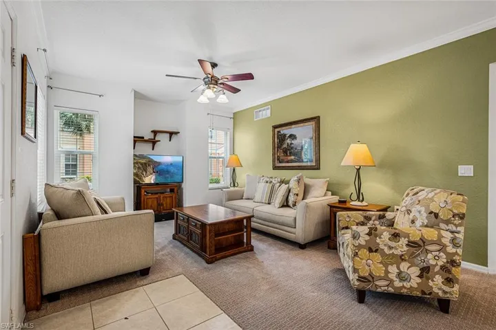 Tiled living area featuring a ceiling fan, carpet, and ornamental molding