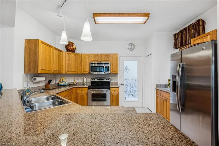 Kitchen with stainless steel appliances, backsplash, brown cabinetry, and pendant lighting