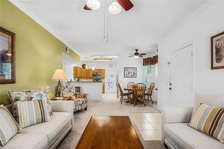 Living area featuring ceiling fan, ornamental molding, light colored carpet, and light tile patterned floors