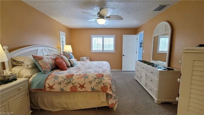 Carpeted bedroom featuring a textured ceiling, visible vents, and a ceiling fan