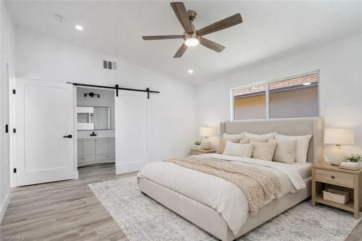 Bedroom with a barn door, lofted ceiling, light wood-type flooring, a ceiling fan, and recessed lighting