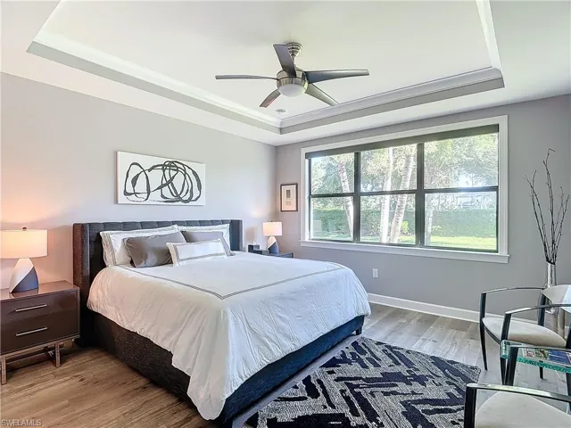 Bedroom featuring hardwood / wood-style floors, crown molding, a tray ceiling, and ceiling fan