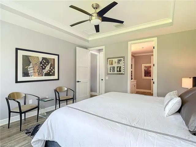 Bedroom featuring light hardwood / wood-style floors, ensuite bath, a tray ceiling, and ceiling fan