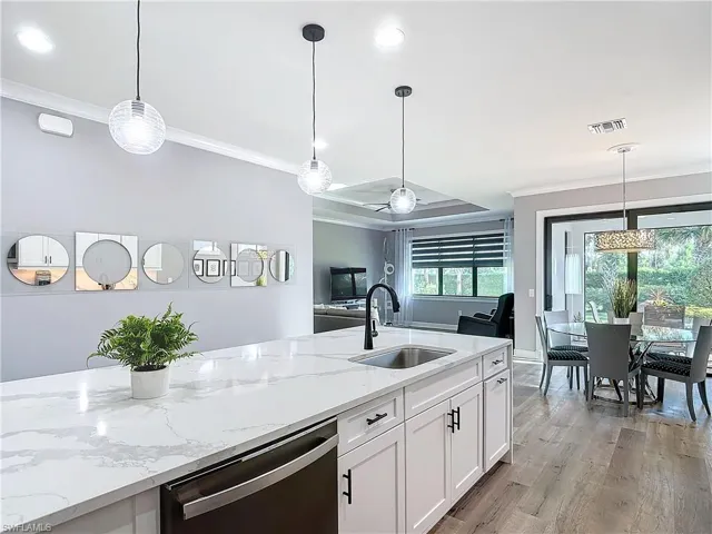 Kitchen featuring white cabinetry, stainless steel dishwasher, pendant lighting, crown molding, and sink
