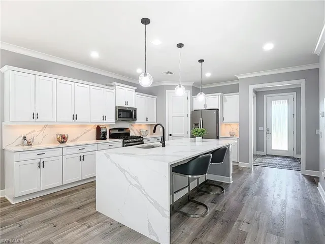 Kitchen with white cabinets, appliances with stainless steel finishes, a kitchen island with sink, hardwood / wood-style flooring, and sink
