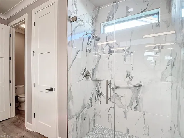Bathroom featuring ornamental molding, a shower with shower door, wood-type flooring, and toilet