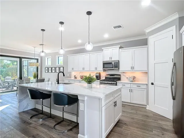 Kitchen featuring white cabinetry, stainless steel appliances, a center island with sink, and sink