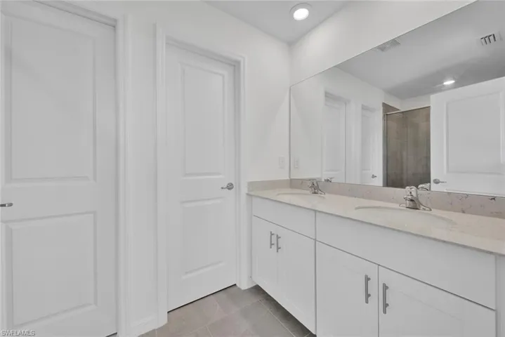 Bathroom featuring double vanity, tiled shower, tile patterned flooring, and recessed lighting
