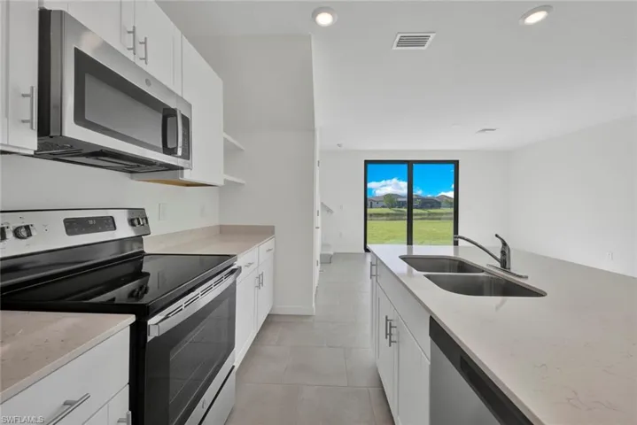 Kitchen featuring appliances with stainless steel finishes, a sink, light stone counters, white cabinets, and recessed lighting