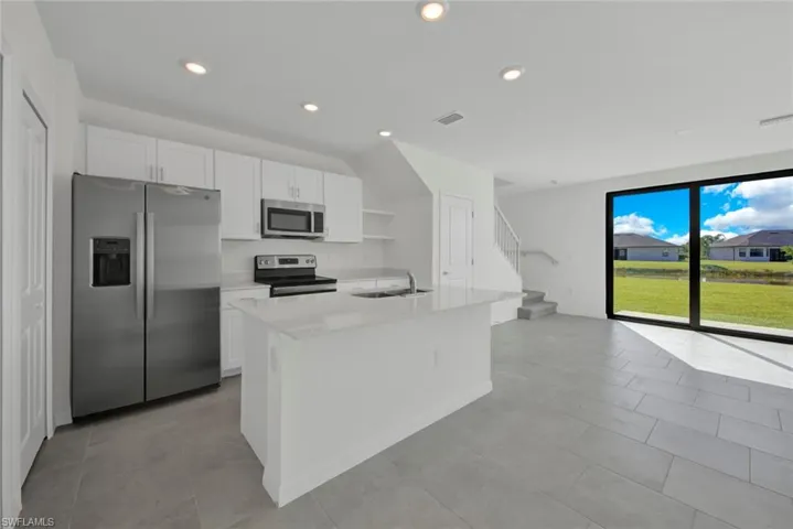 Kitchen featuring appliances with stainless steel finishes, a sink, white cabinets, recessed lighting, and a center island with sink
