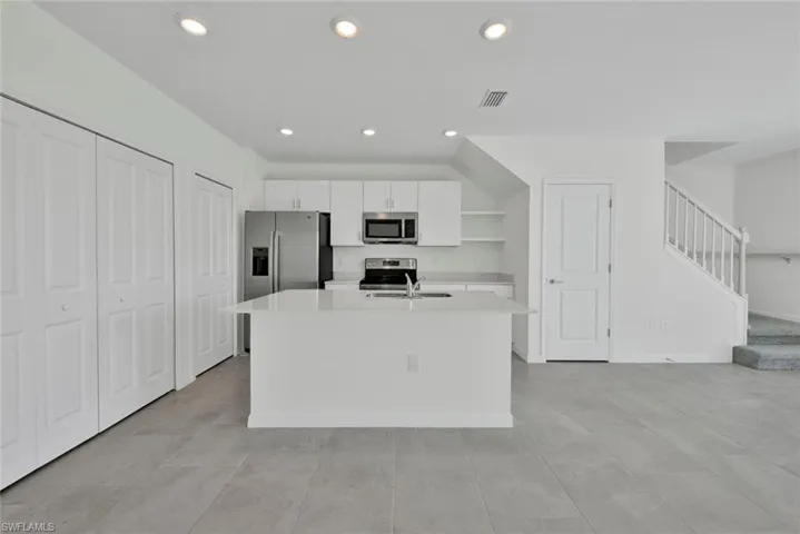 Kitchen featuring appliances with stainless steel finishes, white cabinetry, light countertops, an island with sink, and a sink