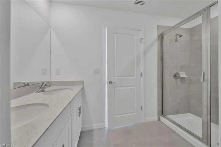 Bathroom with tile patterned floors, double vanity, a shower stall, and baseboards