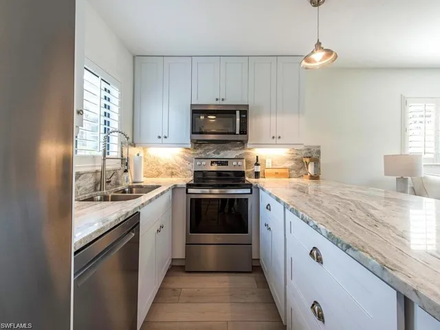 Kitchen with stainless steel appliances, light stone countertops, decorative light fixtures, decorative backsplash, and light wood-style floors