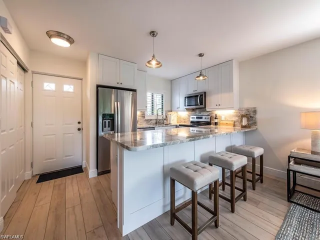 Kitchen with a breakfast bar area, stainless steel appliances, a peninsula, decorative light fixtures, and light stone countertops