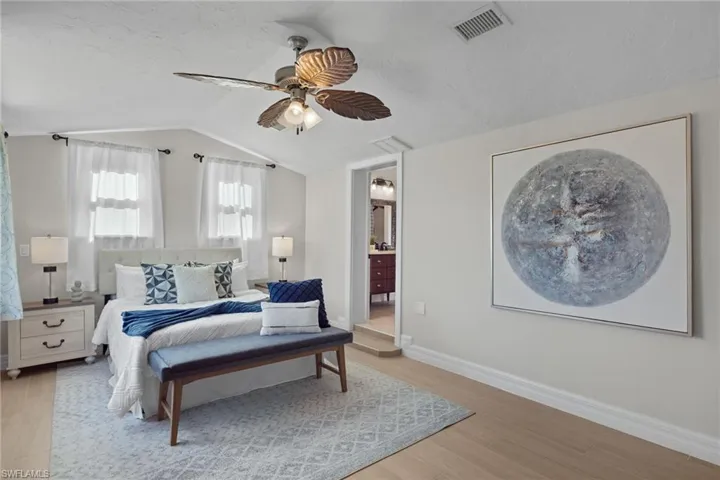 Bedroom with ensuite bath, ceiling fan, light hardwood / wood-style floors, and vaulted ceiling