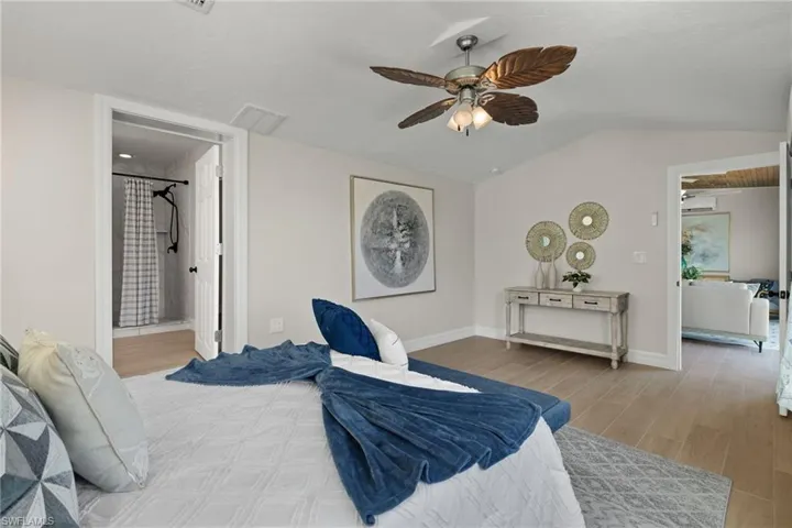 Bedroom with hardwood / wood-style flooring, ensuite bathroom, ceiling fan, and lofted ceiling