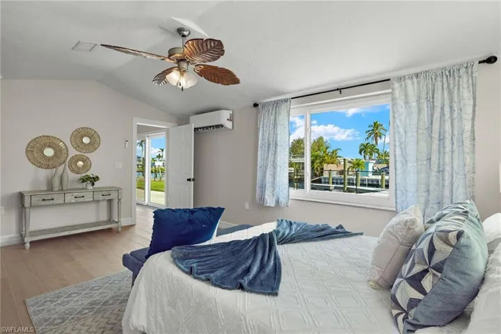 Bedroom with a wall mounted air conditioner, access to exterior, vaulted ceiling, ceiling fan, and light hardwood / wood-style flooring