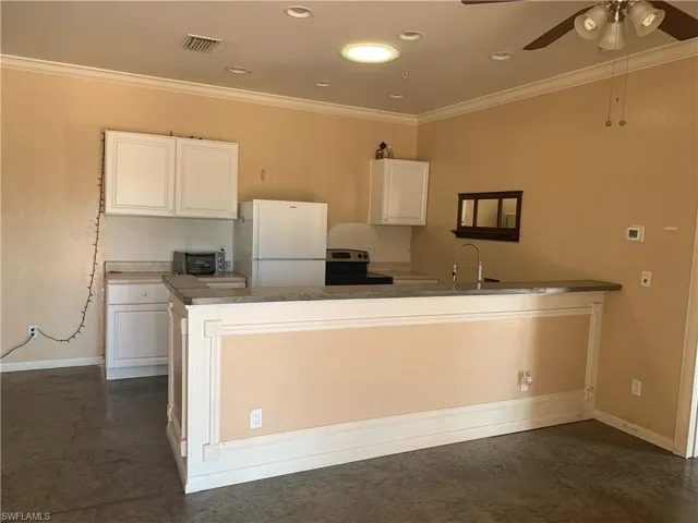 Guest Apartment Kitchen with electric range, white cabinetry, ornamental molding, and freestanding refrigerator