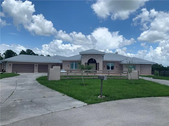 View of front facade with a fenced front yard, stucco siding, a front yard, metal roof, and driveway