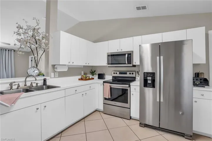 Kitchen featuring white cabinetry, appliances with stainless steel finishes, sink, light tile floors, and lofted ceiling