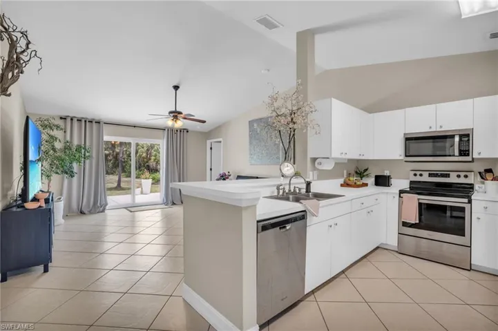 Kitchen featuring appliances with stainless steel finishes, white cabinets, kitchen peninsula, sink, and ceiling fan