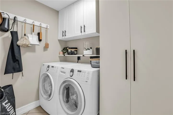 Laundry area featuring electric dryer hookup, separate washer and dryer, light tile flooring, and cabinets