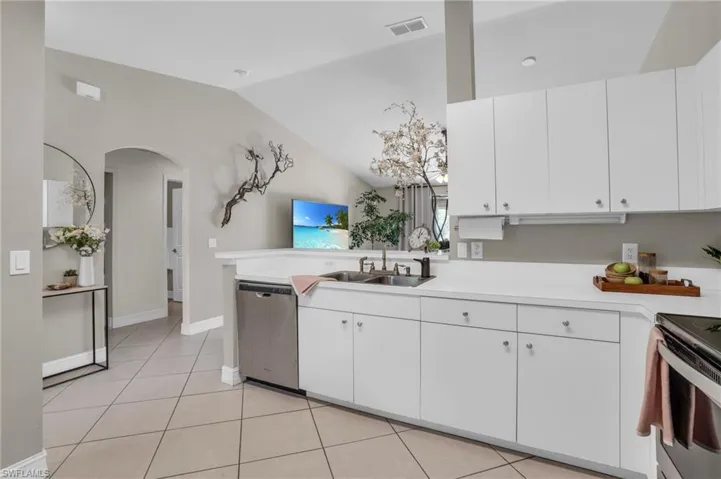 Kitchen featuring stainless steel dishwasher, light tile floors, sink, white cabinets, and lofted ceiling
