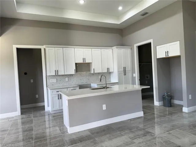 Kitchen featuring a kitchen island with sink, white cabinetry, and backsplash