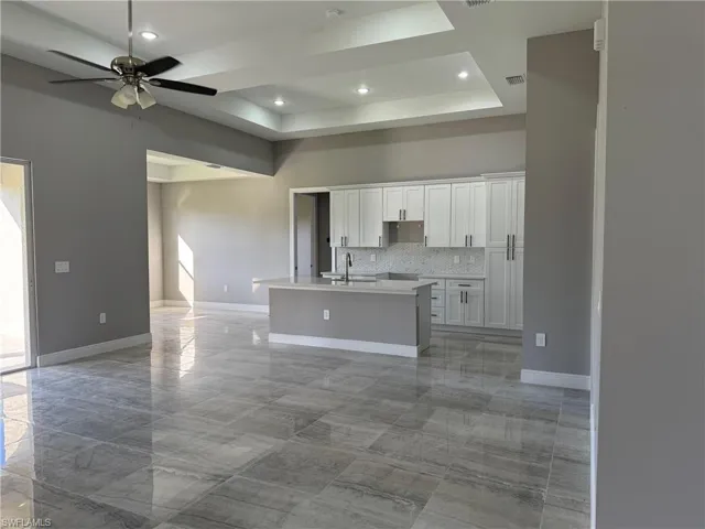 Kitchen with white cabinetry, a center island with sink, tasteful backsplash, a tray ceiling, and ceiling fan