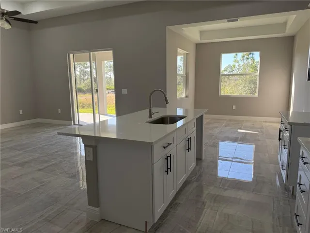 Kitchen featuring light stone counters, a kitchen island with sink, white cabinets, a tray ceiling, and ceiling fan