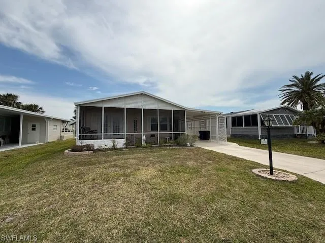 View of front facade featuring a sunroom, concrete driveway, a carport, and a front lawn