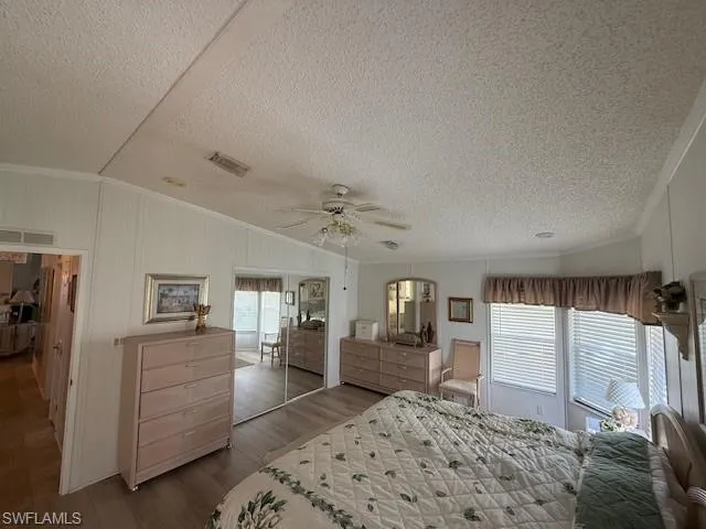 Bedroom featuring vaulted ceiling, multiple windows, wood finished floors, visible vents, and ornamental molding